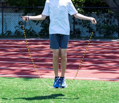 Koşu antrenmanı sırasında yeşil çimlerde ip atlayan bir lise koşucusu..