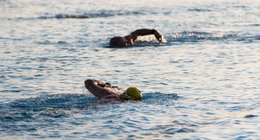 Seçici odaklı bir havuzda üç yüzücü sabah erken saatlerde triatlona hazırlanırken bir ve iki yüzücü bulanıklaşmak için kullanıldı..