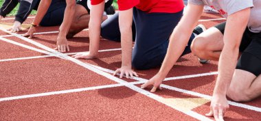 Liseliler başlangıç çizgisinde atletizm koşucuları kırmızı pist ve saha antrenmanında sprint yarışına hazırlar..