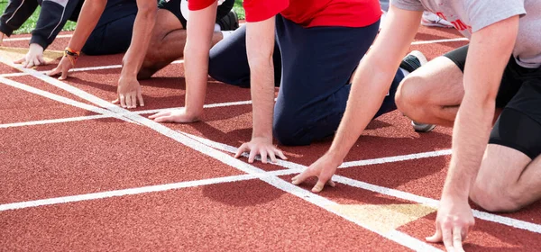 High school boys track and field runners at the starting line ready to start a sprint race in lanes on a red track at track and field practice.