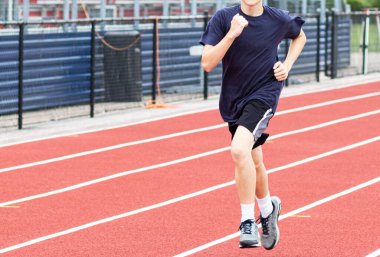 Arka planda tribünlerle kırmızı pistte koşan bir liseli çocuk..