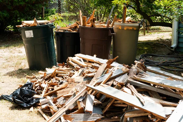 Piles of wood on the ground and in garbage pails left from removing a wood deck in a backyard.