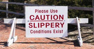 Ahşap bariyerlerde kırmızı yazılar olan büyük beyaz bir tabela lütfen dikkat edin. Güneşli bir günde parkın girişinde kaygan koşullar mevcut..