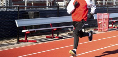 Bir liseli çocuk hipodrom antrenmanında hızlı koşuyor. Parlak gün ışığında eşofman üstü ve eldiven giyiyor..