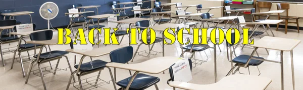A high school class room is set up eith desks separated by six feet with every other desk unavailable to be sat in marked with paper and yellow back to school written.