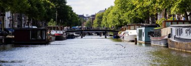 Amsterdam, Hollanda - 5 Ağustos 2025: Sakin sular bereketli bir kentteki ağaçlar ve köprüler boyunca kayıkları yansıtıyor.