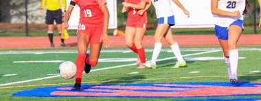 Genç sporcular yeteneklerini güneşli bir futbol sahasında sergiliyorlar..