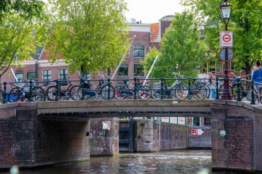 Amsterdam, Hollanda - 45 Ağustos 2025: Bisikletler, yakındaki canlı binaların bulunduğu sakin bir kanala bakan bir köprüde dinleniyor.