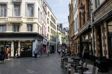 Brüksel, Belçika - 6 Ağustos 2025: İnsanlar çeşitli dükkanlar ve kafelerle dolu bir kaldırım taşı caddesi boyunca yürüyor.