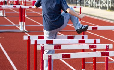 Bir gencin arka görünüşü antrenman sırasında kırmızı bir pistte engelli koşuların üzerinde ayak talimi yapmaktır..