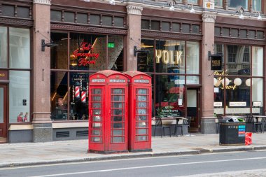 Londra, İngiltere - 7 Ağustos 2025: Bir kafe ve berber dükkanının önündeki kaldırımda iki kırmızı telefon kulübesi.