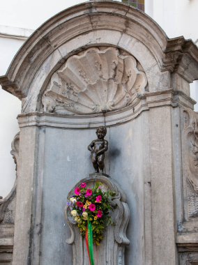 Brüksel, Belçika - 6 Ağustos 2025: Tarihi bir bölgedeki çiçek aranjmanının üzerinde küçük bir bronz heykel duruyor.