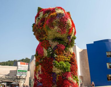 Bilbao, İspanya - 11 Ağustos 2025: Turistler güneşli bir tatil sırasında İspanya 'nın Bilbao kentinde büyük bir çiçek heykelini keşfettiler.