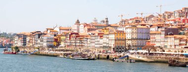 İnsanlar Porto 'da nehir kenarında yürür, binaların ve teknelerin manzarasının tadını çıkarırlar..