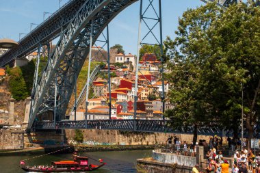 Porto, Portekiz - 13 Ağustos 2025: Ziyaretçiler köprü ve yakınlarındaki evleri seyrederken Porto 'daki nehir kenarının keyfini çıkarıyorlar.