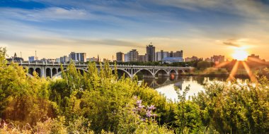 Güney Saskatchewan Nehri 'nin sakin sularının Üniversite Köprüsü' nün altından aktığı Orta Kanada 'daki Saskatoon şehrinin üzerinde ılık bir yaz günbatımı.