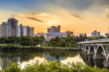 Güney Saskatchewan Nehri 'nin sakin sularının Üniversite Köprüsü' nün altından aktığı Orta Kanada 'daki Saskatoon şehrinin üzerinde ılık bir yaz günbatımı.
