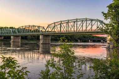 Günbatımının turuncu parıltısıyla yüksek nehir sularının üzerindeki çelik metal köprü..