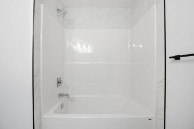 Beyaz küveti ve beyaz duşu olan beyaz bir banyo. Duş boş. Banyo temiz ve bakımlı.