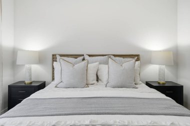 Beyaz yastıklı yatak ve gri bir battaniye. Yastıklar düzgünce yerleştirildi ve yatak yapıldı. Oda aydınlık ve yatak da görüntünün odak noktası.