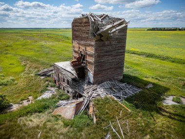 Çimenli bir alanda büyük bir tahıl asansörü. Bina harabe ve bir sürü enkaz var.