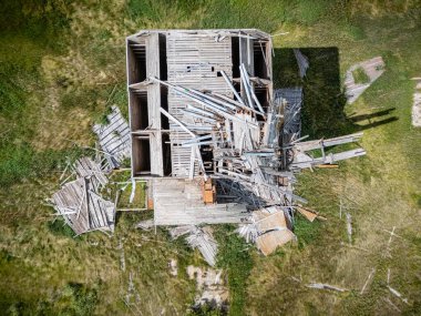 Etrafına bir sürü odun yığını saçılmış tahıl asansörü. Tahıl asansörü çimenli bir araziye yerleştirilmiş ve etrafındaki odun kalıntıları yığılmış.