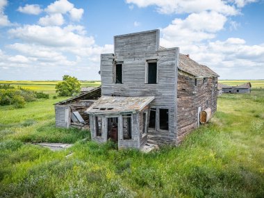 Çok penceresi olan büyük, eski bir bina bir tarlada duruyor. Bina bakımsız durumda ve terk edilmiş durumda. Uzakta bazı ağaçlar ile çevre alan çoğunlukla otlaktır.