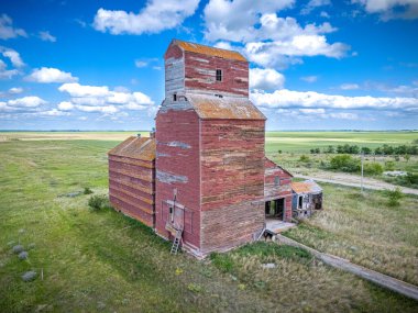 Kırmızı tahıl ambarı bir tarlanın ortasında. Silo eski ve üzerinde çok fazla pas var. Gökyüzü mavi ve arka planda bazı bulutlar var