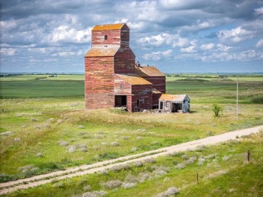 Önünde bir yol olan bir tarlada kırmızı tahıl asansörü duruyor. Ahır eski ve yıpranmış görünüyor. Alan boş ve gökyüzü bulutlu. Sahne huzurlu ve sessiz.