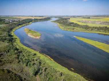 River with a green island in the middle. The water is calm and clear. The sky is blue and there are no clouds