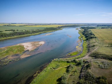 River with a green grassy bank and a blue sky in the background. The water is calm and peaceful