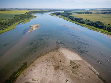 River with a sandy bank and a few trees in the background. The water is calm and clear
