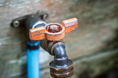 Rusty faucet with a silver handle. The handle is orange and the faucet is old