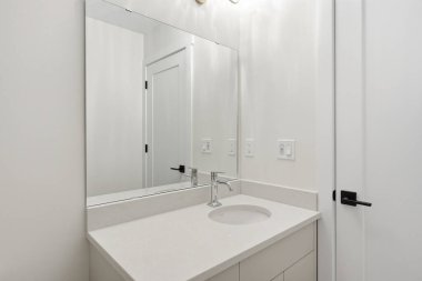 Lavabosu ve aynası olan bir banyo. Ayna kapıyı ve lavaboyu yansıtıyor. Banyo temiz ve bakımlı.