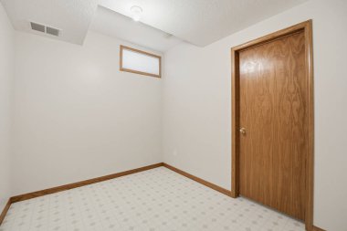 Ahşap kapısı ve penceresi olan küçük bir oda. Oda boş ve düz beyaz bir duvarı var.