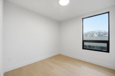 Penceresi ve beyaz duvarı olan küçük, boş bir oda. Oda çıplak ve dağınık. Mobilya ya da dekorasyon yok. Pencere içeri doğal ışık salıyor, parlak ve havadar bir atmosfer yaratıyor.