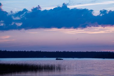 Tekne gün batımında bir gölde yüzüyor. Gökyüzü güzel bir mavi ve pembe karışımıdır.