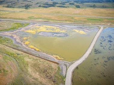 Büyük bir su kütlesi toprak bir yol ve çimenli bir alanla çevrilidir. Su bulanık ve kahverengiye benziyor, sarımsı bir rengi var. Sahne, yalnızlık ve ihmalkârlık hissi veriyor.