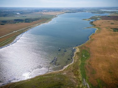 Büyük bir su kütlesi ve kumlu bir kıyı şeridi. Su sakin ve gökyüzü berrak.
