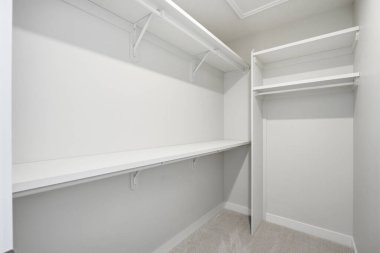 Rafları ve beyaz masası olan beyaz bir dolap. Dolap boş.