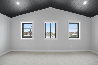 Üç pencereli ve siyah tavanlı bir oda. Pencerelerin hepsi açık. Oda boş.