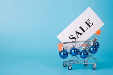 Noel indirimi konsepti. Yan profil, oyuncak mini alışveriş arabasının arka planda boş alanla izole edilmiş mücevherlerle süslenmiş büyük kelime satışı pankartı taşıması.