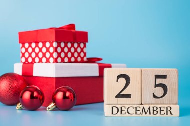 Mutlu Noeller. 25 Aralık 'ı gösteren tahta blok takviminin ve mavi arkaplanda izole edilmiş kırmızı topların fotoğrafını kapat.