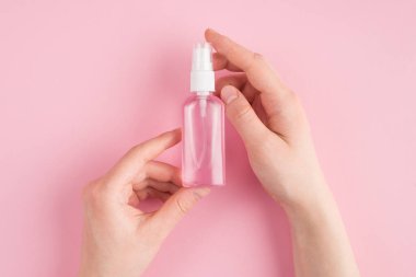 Tepedeki üstte kadın ellerinin fotokopi çekilen pembe pastel arka planda dezenfektan tutarken çekilmiş yakın görüntü fotoğrafı var.