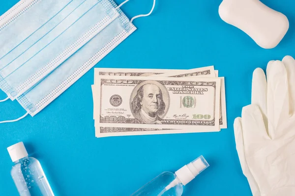 Corona crisis concept. Top above overhead close up flat lay photo of pile of money and hygienic face mask white soap antibacterial liquid gel isolated over blue background