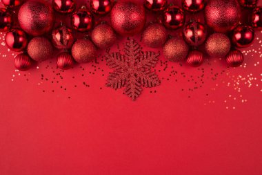 Noel kutlaması kavramı. Tepedeki tepede güzel dekore edilmiş kırmızı süs eşyalarının ve kırmızı arka planda izole edilmiş kırmızı kar tanelerinin yakın plan fotoğrafı var.