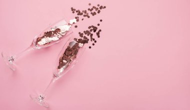 Parti konsepti. Tepeden bakınca iki şampanya flütü dolusu konfetiyi yakın plan pembe arka planda ve kopyalanmış olarak görüyorsunuz.