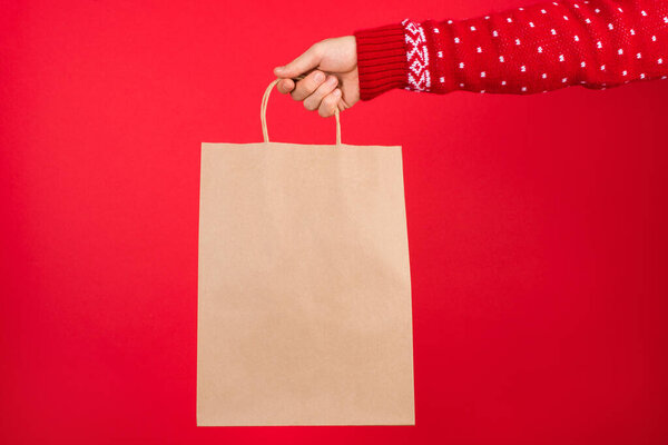 Christmas holidays shopping concept. Close up photo of men in red sweater holding craft paper bag isolated on red background