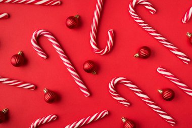 Sert karamelli bastonların ve küçük oyuncak mücevherlerinin izole edilmiş parlak kırmızı arkaplanının üst görüntüsünü kapat