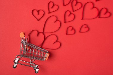 Sevgililer Günü konseptinde alışveriş yapmak. Boş itme arabasının ve uçuşan kırmızı kalplerin izole edilmiş parlak arkaplanın düz bir görüntüsü vardı.